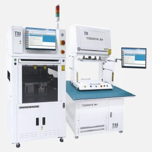 Two large industrial in‑circuit test machines stand side by side, labeled “TR5001E SII INLINE” and “TR5001E SII.” Each unit features a monitor displaying test software, indicator lights, emergency stop buttons, and enclosed testing areas for securing circuit boards. The machines are part of an automated electronics quality‑control setup.